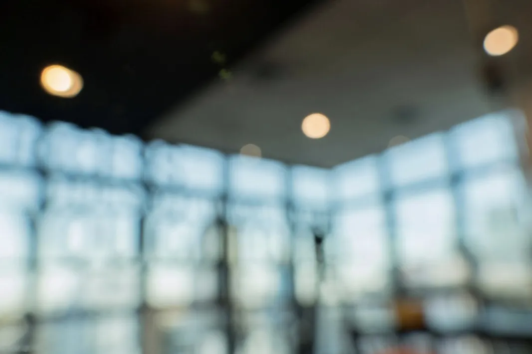 A blurred, sunlit office lobby with floor-to-ceiling glass.