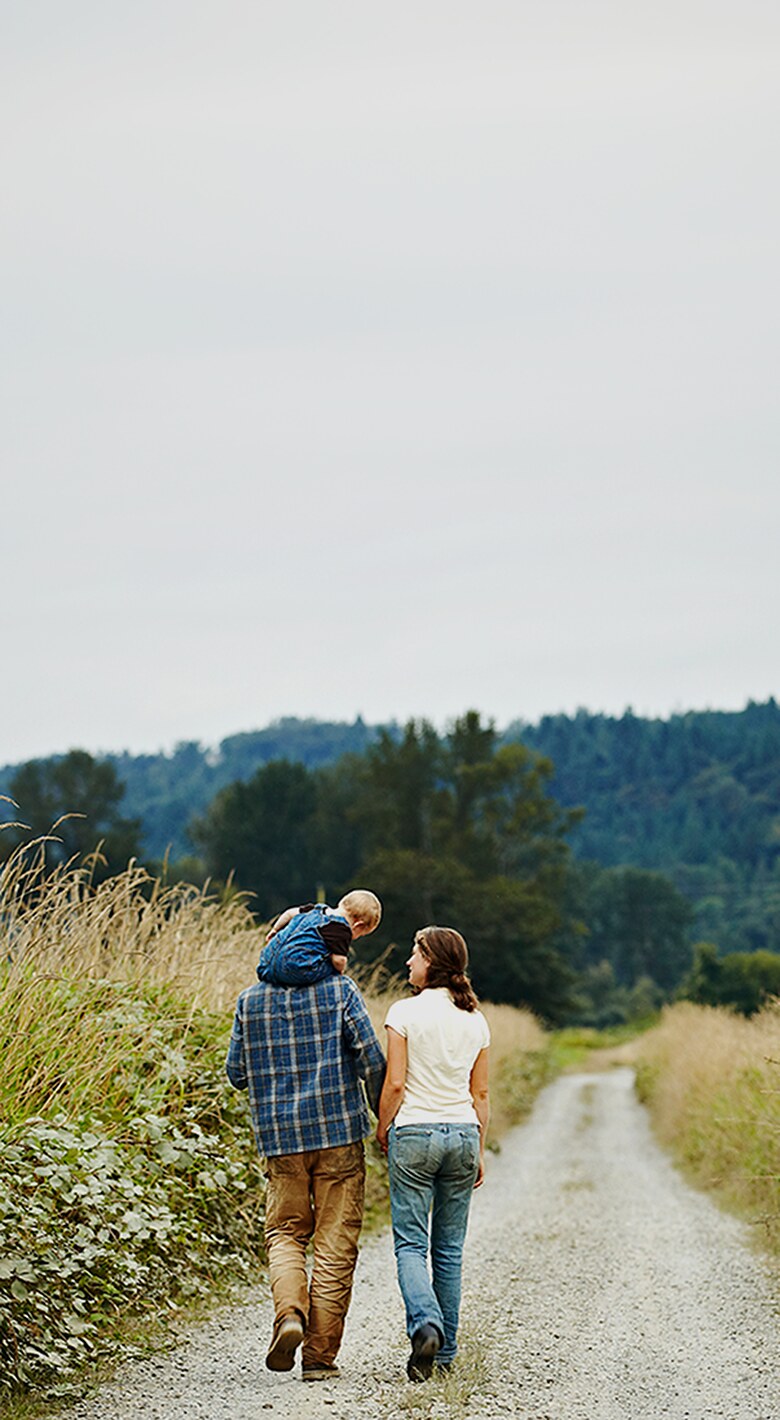 A family walking hand in hand along a gravel path through tall grass.